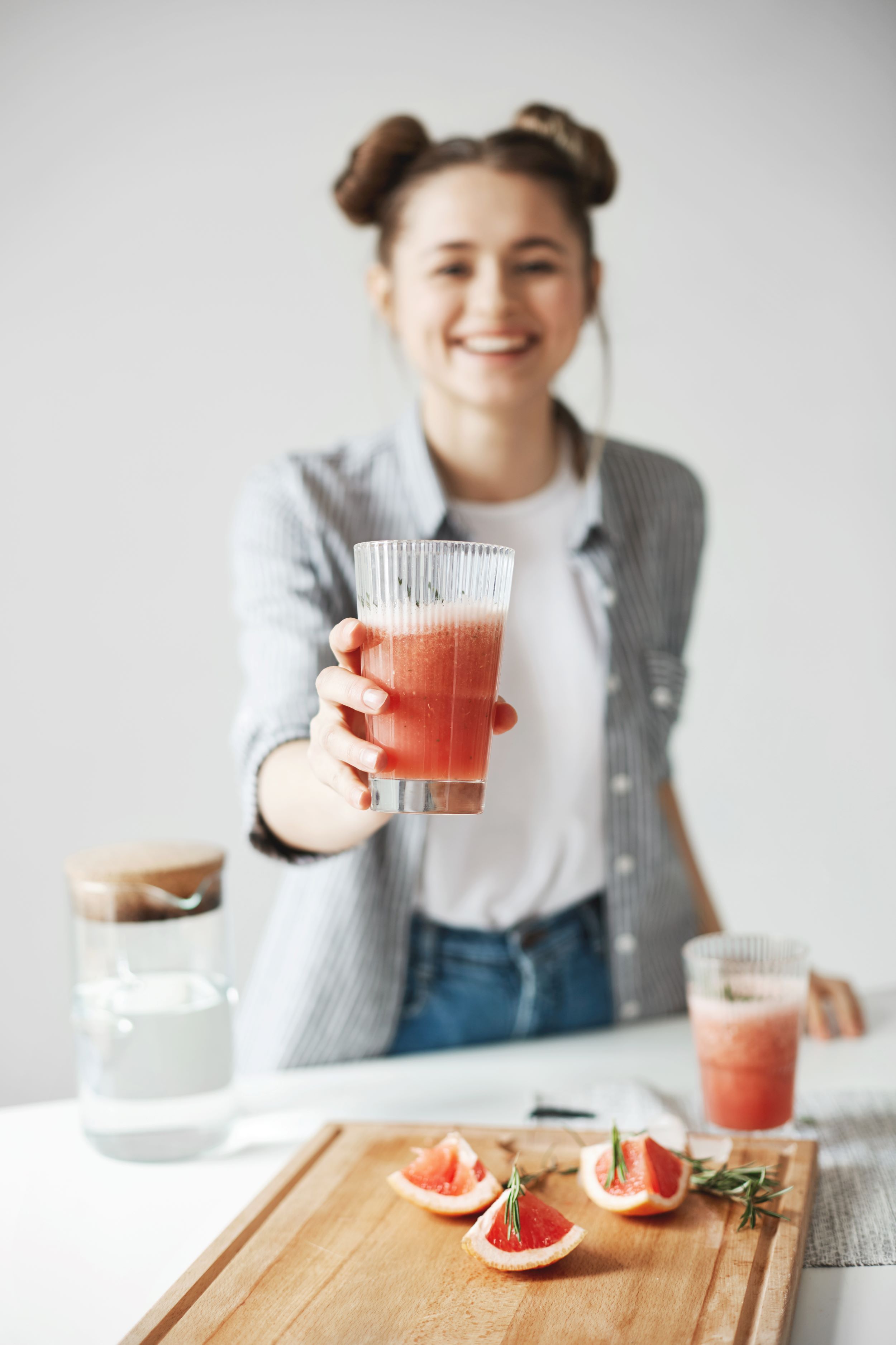 happy-woman-with-buns-smiling-stretching-grapefruit-detox-smoothie-white-wall-healthy-diet-food-focus-glass.jpg