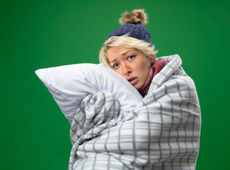 sick-unhealthy-woman-with-short-hair-warm-scarf-hat-feeling-unwell-wrapped-blanket-holding-pillow-looking-camera-with-sad-expression-standing-purple-background_141793-48946.jpeg