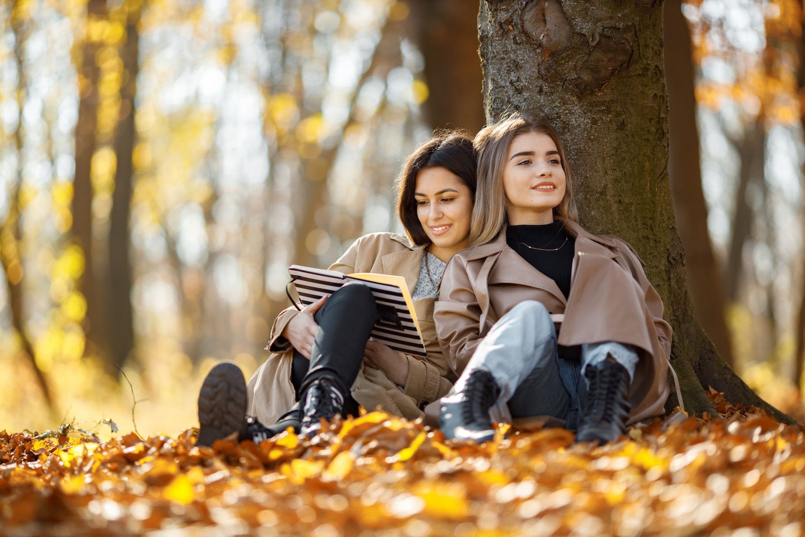 two-beautiful-female-friends-spending-time-together-two-young-smiling-sisters-sitting-near-tree-reading-book-brunette-blonde-girls-wearing-coats.jpg