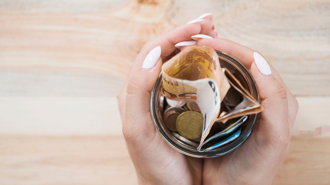 woman-s-hand-holding-glass-jar-with-euro-notes-coins-wooden-backdrop.jpg