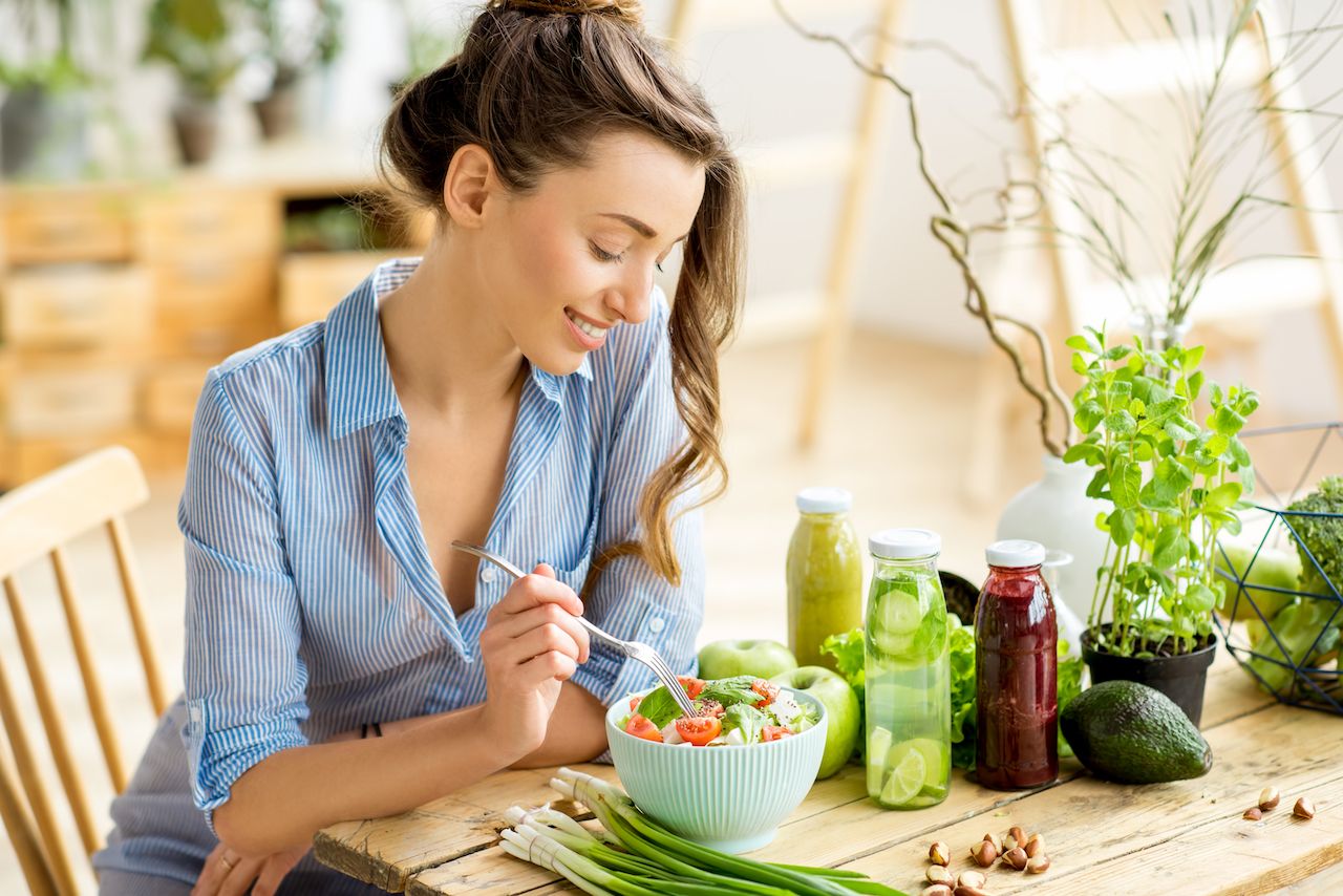 young-happy-woman-eating-healthy-salad-sitting-table-with-green-fresh-ingredients-indoors.jpg